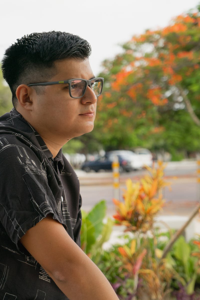 Relaxed man with glasses in a Yucatan park surrounded by vibrant flora.