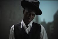 Close-up moody portrait of an African American man in a fedora hat and black vest.